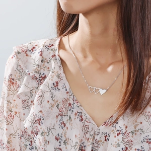 Dettaglio di una collana con tre cuori intrecciati indossata su un abito a fiori elegante