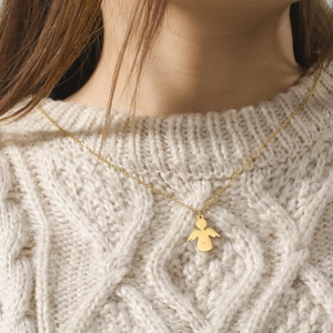 Minimalist gold angel pendant necklace shown on a model wearing a beige sweater