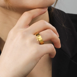 Polished gold wide stainless steel ring with a hanging cross charm on finger