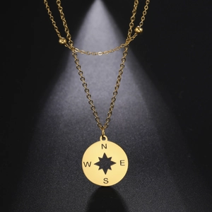 Detail van gouden dubbellaagse kompas ketting met holle ster en gegraveerde N S W E
