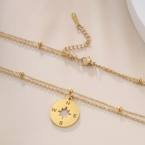 Detail van een gouden dubbele ketting met kompasster hanger en kleine metalen kralen