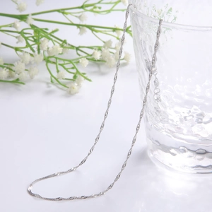 Detailed view of silver water wave chain necklace draped over a textured glass cup