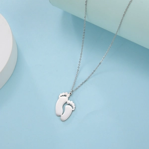 Polished metal baby footprint pendant necklace on light blue minimalist background