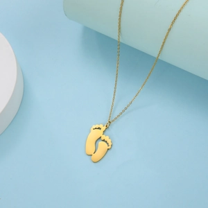 Detail of a golden baby feet pendant necklace on a blue and white geometric background