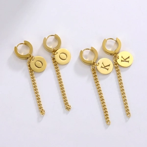 Détail de boucles d'oreilles en acier titane doré avec breloques lettres et chaînes