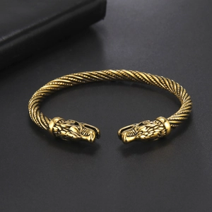 Dettaglio delle teste di lupo intagliate su un bracciale rigido a fune in acciaio dorato