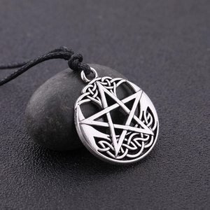 Detailed close-up of retro silver pentagram pendant with Celtic knot on a dark pebble