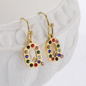 Détail de la boucle d'oreille lettre Q dorée ornée de strass colorés sur fond blanc