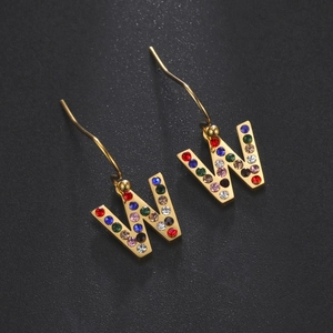 Détail de boucles d'oreilles lettre W dorées avec strass multicolores sur noir