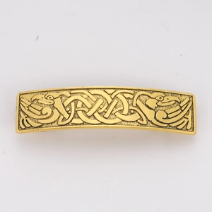 Macro detail of golden metal barrette featuring embossed bird and Celtic knot patterns