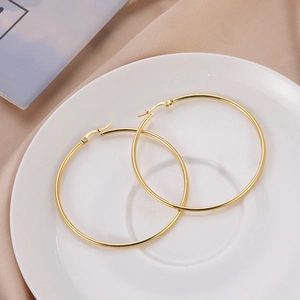 Detailed top view of large polished gold hoop earrings on white porcelain and pink silk