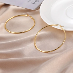 Detail view of large gold hoop earrings with latch closure on elegant champagne satin fabric