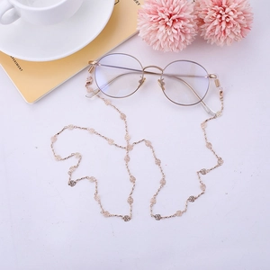 Chaîne de lunettes dorée avec maillons roses évidés présentée sur un bureau élégant