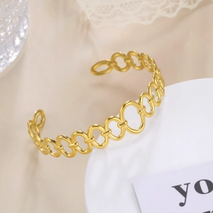 Detailed view of an 18k gold-plated stainless steel oval link cuff bracelet on porcelain