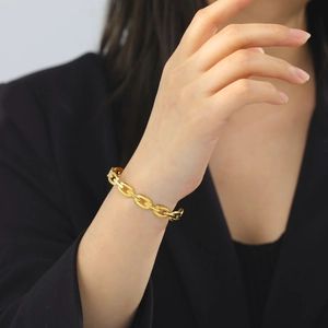 Detail of gold-plated oval link chain bracelet on wrist over a black suit background