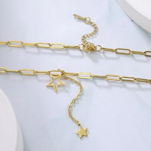 Close-up of gold paperclip chain necklace with hollow and solid star charms on marble