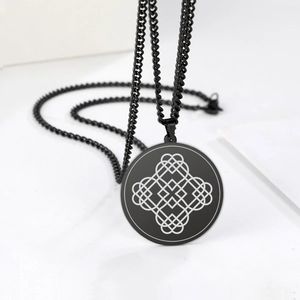 Dettaglio macro del ciondolo talismano nero con motivo a nodo geometrico bianco sulla catena