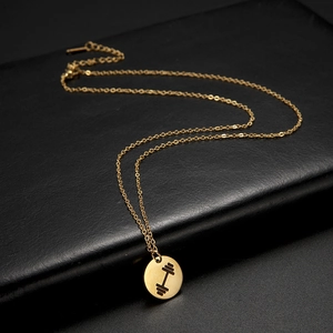 Detailed close-up of golden stainless steel dumbbell pendant on black leather texture