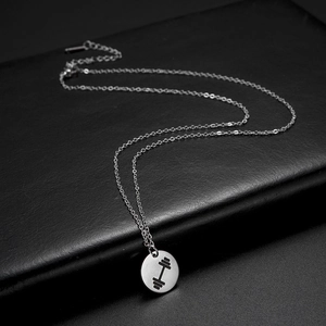 Detailed view of silver barbell pendant on a fine link chain against black leather