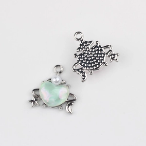 Détail d'un pendentif cœur argenté avec résine verte, perle et motifs étoile et lune