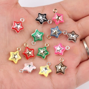 Colorful star-shaped enamel pendants for DIY jewelry making held in a palm for scale