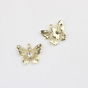 Détail de breloques papillon dorées avec ailes évidées et cristal en forme de cœur