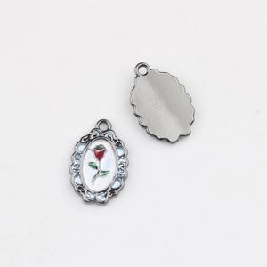 Macro view of oval rose charm pendant showing floral enamel front and metallic back
