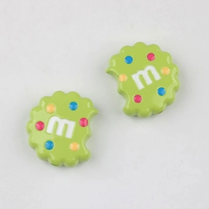 Close-up of green cookie shaped resin charms with m letter and colorful dot patterns