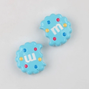 Macro view of blue acrylic cookie charms with colorful dots and letter M for DIY crafts