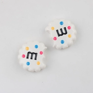 Macro detail of bitten cookie acrylic beads with colorful dots and letter M for DIY