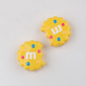 Macro shot of yellow cookie charm with m letter and colorful dots for DIY crafts