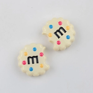 Macro detail of cream-colored cookie resin charms with M-letter and colorful dots