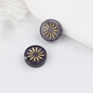 Nahaufnahme violetter tschechischer Glasperlen mit goldener Blumengravur für DIY Schmuck