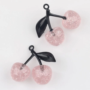 Close-up of pink glitter cherry charms with black leaves for DIY jewelry making