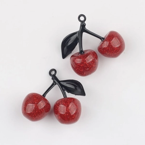 Close-up of glittery red cherry pendants with black leaves for DIY jewelry making