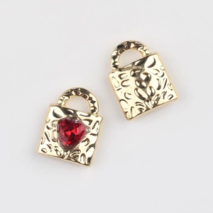 Detail of hammer-textured gold alloy lock pendants with red heart zircon inlay for DIY