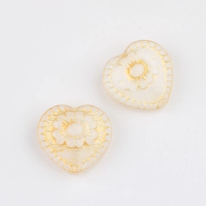 Detailed close-up of heart-shaped Czech glass beads with gold floral engraving and borders