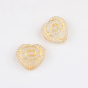 Macro view of heart-shaped Czech glass beads with gold floral etching for DIY crafts