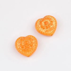 Detailed macro view of orange heart-shaped glass beads with intricate golden flower patterns
