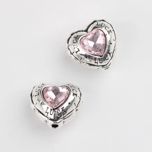 Macro shot of silver heart charm with pink zircon and Luck engraving for DIY jewelry