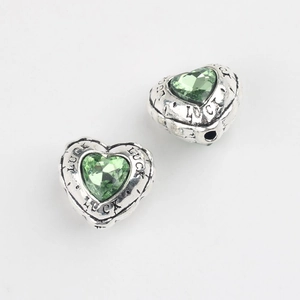Detail of vintage silver heart charm with green zircon inlay and Luck engraving