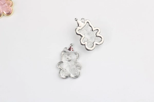 Detail von niedlichem Bären-Anhänger mit rotem Punkthut und Metallrahmen für DIY-Schmuck
