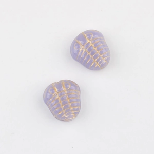 Dettaglio macro di perline in vetro ceco viola con incisione di trilobite dorata