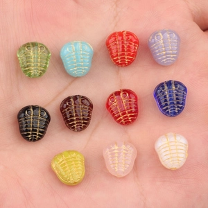 Perline in vetro ceco a forma di trilobite con dettagli dorati mostrate sulla mano