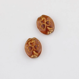 Macro shot of amber glass oval beads featuring golden clover patterns on a white background