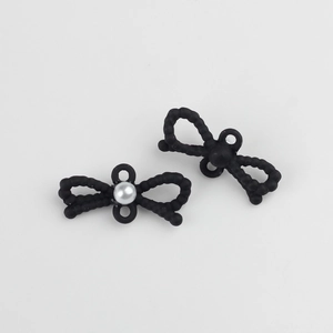 Detalle macro de dijes de lazo negro con acabado mate y adorno de perla blanca