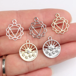 Five hollow alloy pendants with mandala and sun designs held on a finger for scale