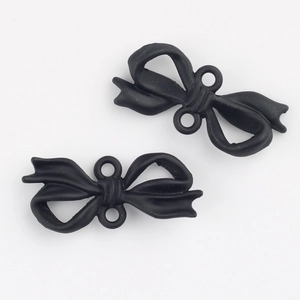 Close-up of matte black bow-shaped charms with dual connector loops for DIY jewelry