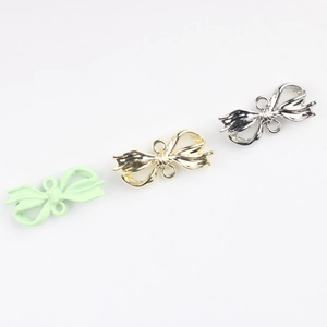 Macro shot of bow-shaped jewelry connectors in matte mint green, gold, and silver finishes