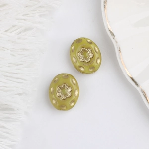 Detail of olive green Czech glass beads with gold floral patterns on a white fabric background